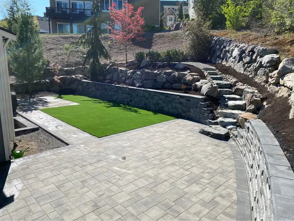 Boulder retaining wall above a paver patio and turf lawn