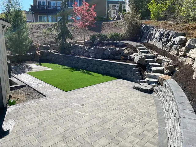 Boulder retaining wall above a paver patio and turf lawn